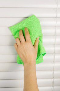 Vertical photo of female hand cleaning window blinds with microfiber cloth